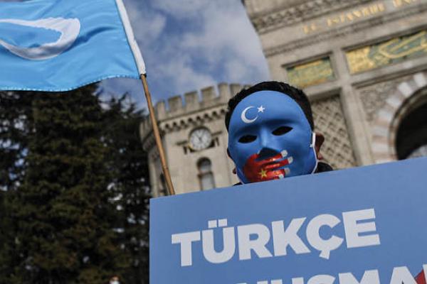 A demonstrator wearing a mask painted with the colors of the flag of East Turkestan holds a placard reading "Speaking Turkish, banned." during a protest by supporters of the Uyghur minority on April 1, 2021, at Beyazid Square in Istanbul.  (Getty Images)