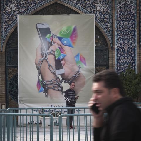 An Iranian man holding his smartphone looks on while standing under an anti-Social networking banner in Tehran Grand Bazaar (Market), December 3, 2022. (Photo by Morteza Nikoubazl/NurPhoto via Getty Images)
