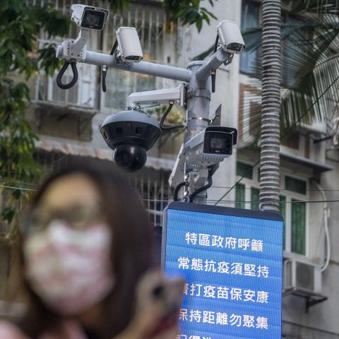 A woman wearing face mask walks in front of a dozen of CCTV Camera on December 29, 2022 in Macau, China. (Photo by Vernon Yuen/NurPhoto via Getty Images)