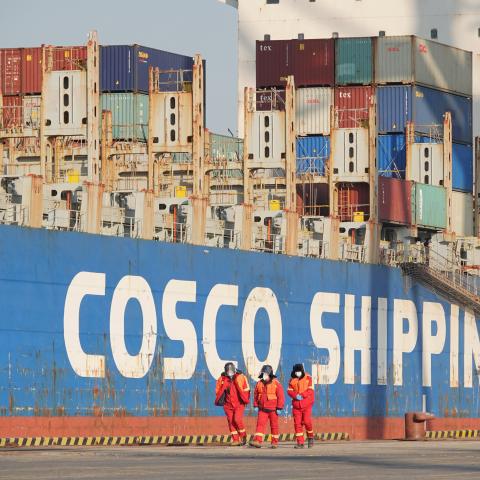 Dockworkers walk past a Cosco Shipping container ship at the Chinese port of Yantai on December 29, 2022. (CFOTO/Future Publishing via Getty Images)