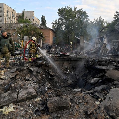 Firefighters push out a fire as police experts look for fragments of missile at a crater on an industrial area of the Ukrainian capital of Kyiv, after a massive overnight missile attack to Ukraine on September 21, 2023. (Sergei Supinkey/AFP via Getty Images)