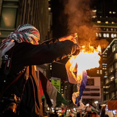 A pro-Palestine supporter burns an Israeli flag during a rally near the Rockefeller Center Christmas Tree Lighting on November 29, 2023, in New York City. (David Dee Delgado via Getty Images)