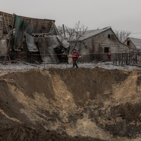 Communal workers walk next to a crater and destroyed houses following a Russian shelling in Kyiv on December 11, 2023. (Roman Pilipey/AFP via Getty Images)