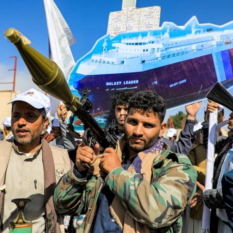A sign depicting a cutout of the Bahamas-flagged cargo vessel Galaxy Leader, which was seized by fighters of Yemen's Huthi movement in late 2023, is raised by a protester behind a man carrying a rocket-propelled grenade (RPG) launcher during a pro-Palestinian rally in the Huthi-held capital Sanaa on February 7, 2024 amid the ongoing conflict in the Gaza Strip between Israel and the Palestinian militant group Hamas. (Photo by MOHAMMED HUWAIS / AFP) (Photo by MOHAMMED HUWAIS/AFP via Getty Images)