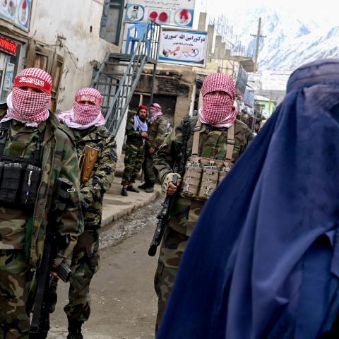 Taliban security personnel stand guard as a burqa-clad woman walks along a street at a market in the Baharak district of Badakhshan province. (Wakil Kohsar/AFP via Getty Images) 
