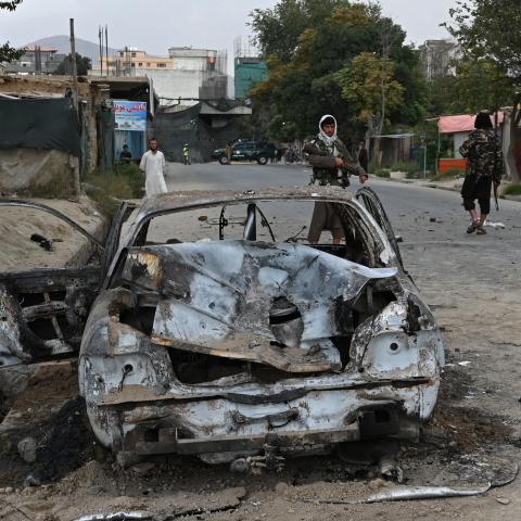 Taliban fighters stand guard near a damaged car after multiple rockets were fired in Kabul on August 30, 2021. (Photo by Wakil Kohsar/AFP via Getty Images)