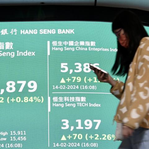 A pedestrian walks by a large electronic screen displaying the numbers for the Hang Seng Index on February 14, 2024, in Hong Kong, China. (Photo by Li Zhihua/China News Service/VCG via Getty Images)