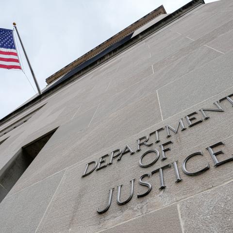 The US flag flies above a sign marking the US Department of Justice headquarters on January 20, 2024, in Washington, DC. (Photo by J. David Ake/Getty Images)