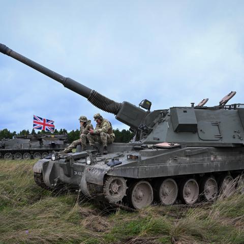  British soldiers sit on a AS90 155mm self-propelled gun as Ukrainian artillery recruits undergo a live fire training exercise, on July 27, 2023 in South West, England. The UK was the first country to donate Western main battle tanks by gifting a squadron of Challenger 2 tanks with armoured recovery and repair vehicles, as well as a battery of eight AS90 guns at “high readiness” and a further two batteries at “varying states of readiness.” The AS90 is an agile, highly accurate, modern artillery system which