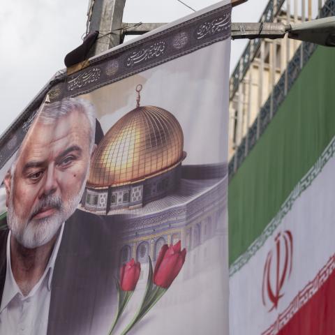 A banner featuring a portrait of Hamas leader Ismail Haniyeh is being hung next to an Iranian flag during a funeral for him and his bodyguard Abu Shaaban in Tehran, Iran, on August 1, 2024. Ismail Haniyeh and his bodyguard, Abu Shaaban, are being killed in an air strike on Haniyeh's residence in northern Tehran the day after the inauguration ceremony of Iran's new president, Masoud Pezeshkian. (Photo by Morteza Nikoubazl/NurPhoto via Getty Images)