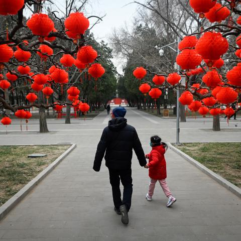 A man and a child walk along a road with red lanterns hanging on trees for the upcoming Chinese Lunar New Year celebrations at a park in Beijing on January 11, 2023. (Wang Zhao/AFP via Getty Images)