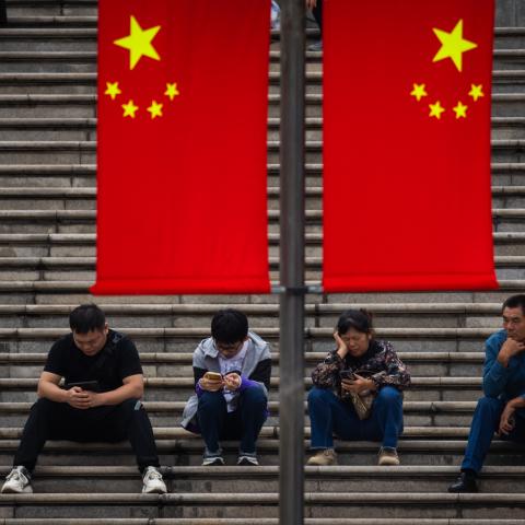 People sit on the steps under Chinese national flags on October 5, 2024, in Chongqing, China. (Cheng Xin via Getty Images)