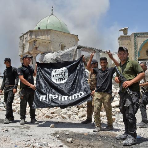 A member of the Iraqi Counter-Terrorism Service raises the victory gesture as others hold upside-down the black flag of the Islamic State in Mosul, Iraq, on June 30, 2017. (Fadel Senna/AFP via Getty Images)