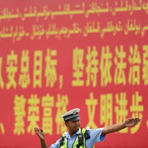 A police officer gestures in front of a propaganda billboard urging "the maintenance of rule of law in Xinjiang" in both Chinese and Uyghur languages in China's northwestern Xinjiang region on July 19, 2023. (Pedro Pardo/AFP via Getty Images)