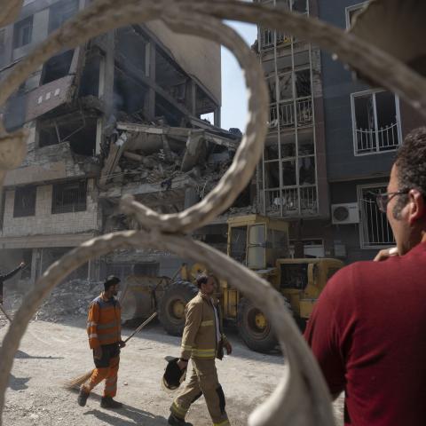 Iranian workers walk past a destroyed residential building due to Israeli attacks in Tehran, Iran, on June 13, 2025. (Photo by Morteza Nikoubazl/NurPhoto via Getty Images)
