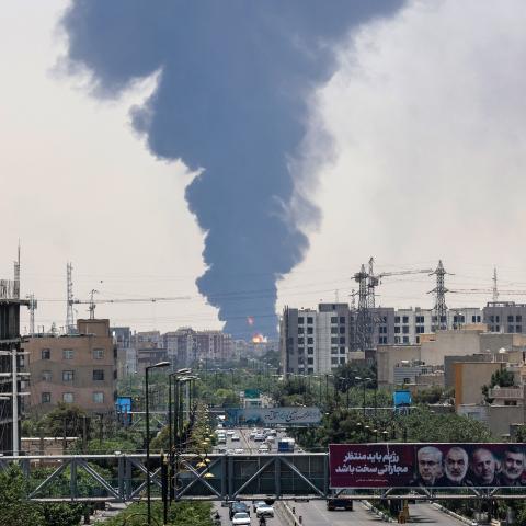 Portraits of Iranian military generals and nuclear scientists killed in Israel’s June 13 attack are displayed above a road as a plume of heavy smoke and fire rise over an oil refinery in southern Tehran on June 15, 2025. (Atta Kenare via Getty Images)