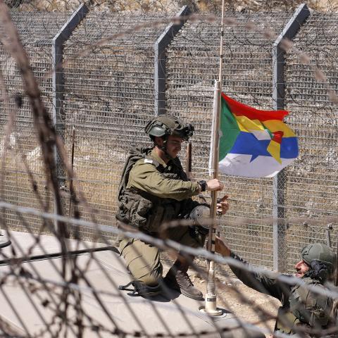 An Israeli soldier attaches a Druze flag to the antenna of a Humvee along a barbed-wire fence in the Golan Heights near the Druze village of Majdal Shams on July 19, 2025. (Jalaa Marey via Getty Images)