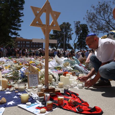 A mourner lights candles as people gather around floral tributes outside Bondi Pavilion in Sydney on December 17, 2025. (Getty Images) Share to Twitter
