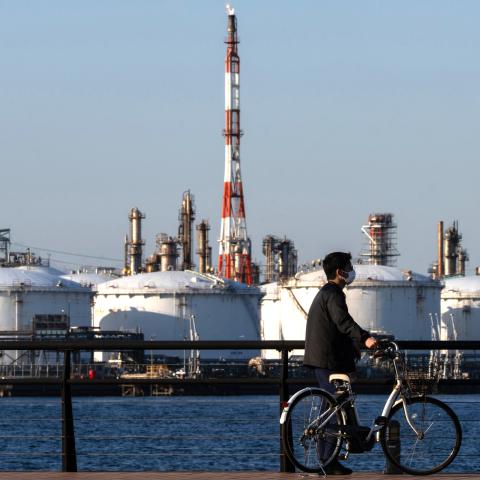 A man pushes his bicycle in front of oil storage tanks at a refinery on March 12, 2026, in Kawasaki, Kanagawa Prefecture, Japan. (Getty Images)