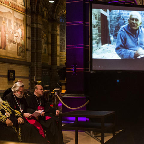 Clerics sit next to a screen showing Dutch priest Frans van der Lugt during a remembrance ceremony for the dead priest in the Sint Nicolaasbasiliek in Amsterdam, on April 11, 2014. (REMKO DE WAAL/AFP/Getty Images)