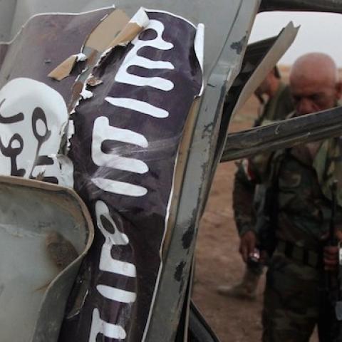 Peshmerga fighters inspect the remains of a car bearing an image of the trademark jihadist flag, north of Mosul, August 18, 2014. (AHMAD AL-RUBAYE/AFP/Getty Images)
