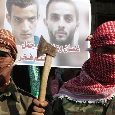 Palestinians celebrate an attack on a Jerusalem synagogue while standing in front of a poster of the attackers in the southern Gaza Strip on November 18, 2014. (SAID KHATIB/AFP/Getty Images)