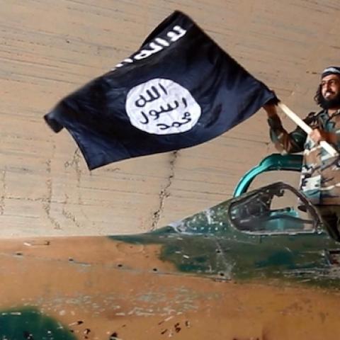 Islamic State fighter waving a flag while standing on a captured government fighter jet in Raqqa, Syria, 2015. (Universal History Archive/UIG via Getty Images)