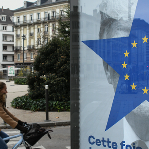 A cyclist rides near a street poster depicting the twelve-star circle from the European Union flag within a blue five-pointed star covering the face of what is deemed to be a portrait of US President Donald Trump. (SEBASTIEN BOZON/Getty Images)