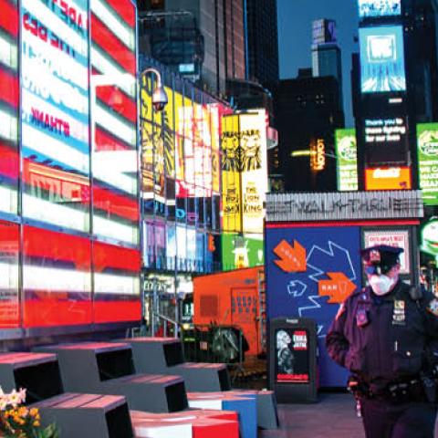 An NYPD officer wearing a protective mask walks past an American Flag in an empty Times Square at night amid the coronavirus pandemic on April 22, 2020 in New York City.