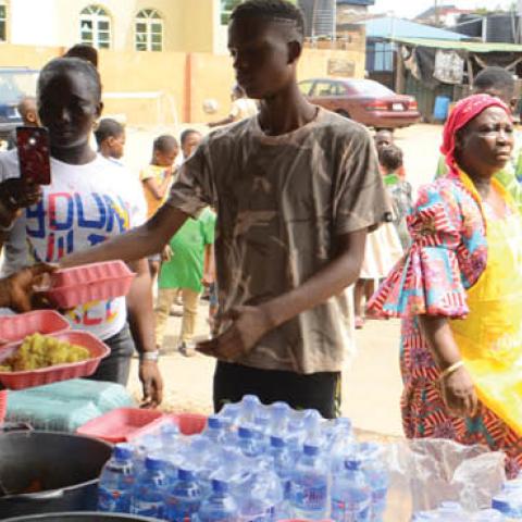 A food vendor serving food as people queue in line to collect food as Lagos state government begins distribution of meals to Youths in verious LCDAs, Local Community Development Areas as part of measures to prevent the spread of COVID-19 in Lagos, on Apri