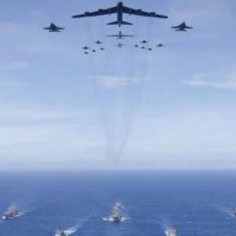 The aircraft carrier USS Ronald Reagan (CVN 76), foreground, leads a formation of Carrier Strike Group Five ships as Air Force B-52 Stratofortress aircraft and Navy F/A-18 Hornet aircraft pass overhead for a photo exercise during Valiant Shield 2018 in th