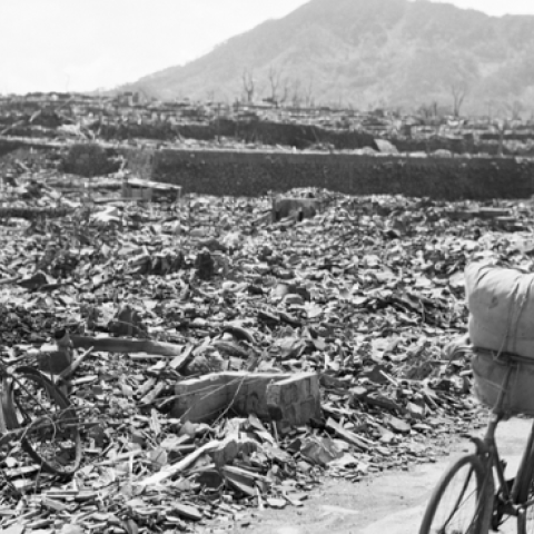 09/13/1945-A Japanese civilian pushes his loaded bike down a path which has been cleared of rubble. On either side of the path debris, twisted metal, and gnarled tree stumps fill the area. (Getty Images)