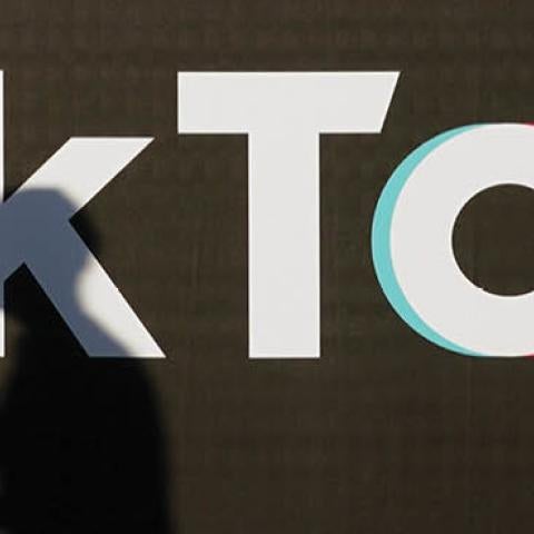 A young man holding a smartphone casts a shadow as he walks past an advertisement for social media company TikTok on September 21, 2020 