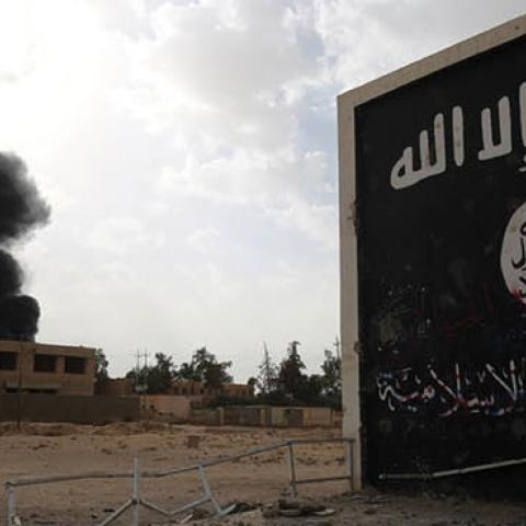 Iraqi fighters of the Hashed al-Shaabi stand next to a wall bearing the Islamic State group flag as they enter the city of al-Qaim, in Iraq's western Anbar province near the Syrian border (AHMAD AL-RUBAYE/AFP via Getty Images)