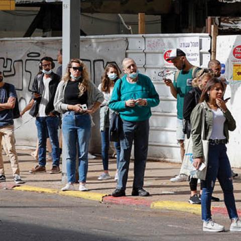 People wait for the bus on a street in the Israeli coastal city of Tel Aviv on April 18, 2021 (Photo by JACK GUEZ/AFP via Getty Images)