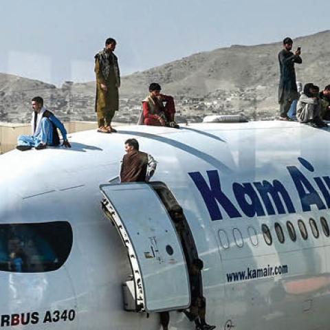Afghan people climb atop a plane as they wait at the airport in Kabul on August 16, 2021 (Photo by WAKIL KOHSAR/AFP via Getty Images)