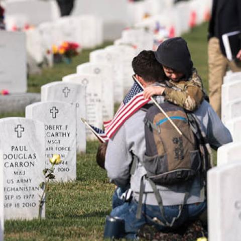 Army veteran Stephen Hedger is hugged by his son Lincoln as he visits the gravesite of U.S. Army Major Paul Douglas Carron at Arlington National Cemetery on Veterans Day, November 11, 2021 in Arlington, Virginia. (Photo by Anna Moneymaker/Getty Images)