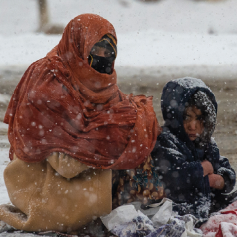 An Afghan woman begs for money from passing cars in the snow, with her child huddled beside her, on the Kabul road south to Pul-e Alam, Afghanistan, on January 17, 2022. (Scott Peterson/Getty Images)